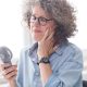 A woman sits at her desk looking uncomfortable, while using a handheld fan to cool down