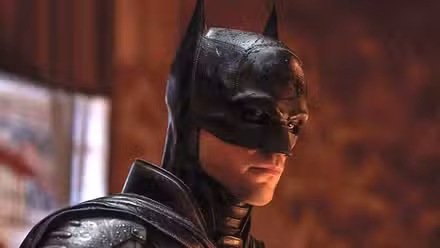 Robert Pattinson as Batman looks down at something in the rain in The Batman.