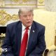 Donald Trump sits in the Oval Office wearing a navy blue suit and red tie.