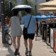 two people walking in the street holding umbrellas to shield them from the hot weather