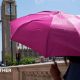 A person shielding from the Sun under an umbrella with the Houses of Parliament in the background