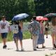 people walking on a pathway through a park.  Some are holding umbrellas to shade them from the hot weather