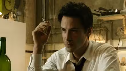 John Constantine (Keanu Reeves) sits at a table smoking in 'Constantine'