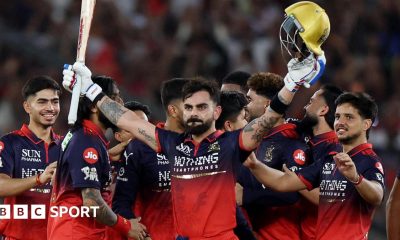 Virat Kohli holds his bat and helmet aloft as his RCB team-mates celebrate winning the IPL
