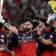 Virat Kohli holds his bat and helmet aloft as his RCB team-mates celebrate winning the IPL
