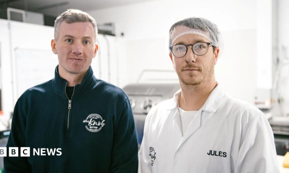 Kieran Woods is wearing a blue fleece with the Knob of Butter logo on it. He is standing next to Jules Bal who is   wearing a hair net, glasses and a white T-shirt with a white overall over it. It has the name Jules sewn into it.