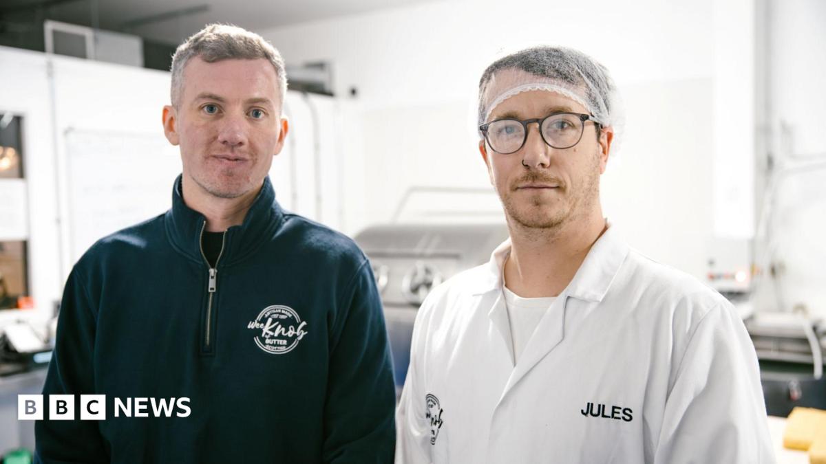 Kieran Woods is wearing a blue fleece with the Knob of Butter logo on it. He is standing next to Jules Bal who is   wearing a hair net, glasses and a white T-shirt with a white overall over it. It has the name Jules sewn into it.
