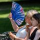 two women sitting on a park bench.  One eating an ice cream, the other fanning herself in the hot weather