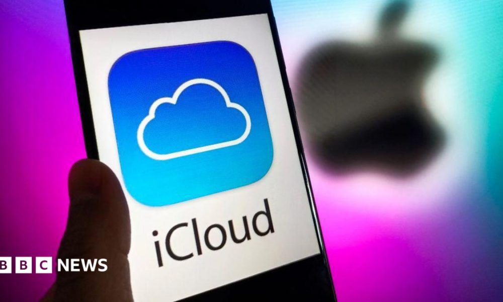 A phone with the words iCloud in black letter, and the iCloud blue and white logo of a cloud on it, against a white background. A blurred Apple logo in black is behind it against a purple background.