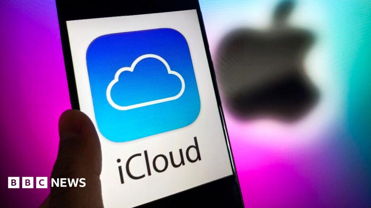 A phone with the words iCloud in black letter, and the iCloud blue and white logo of a cloud on it, against a white background. A blurred Apple logo in black is behind it against a purple background.
