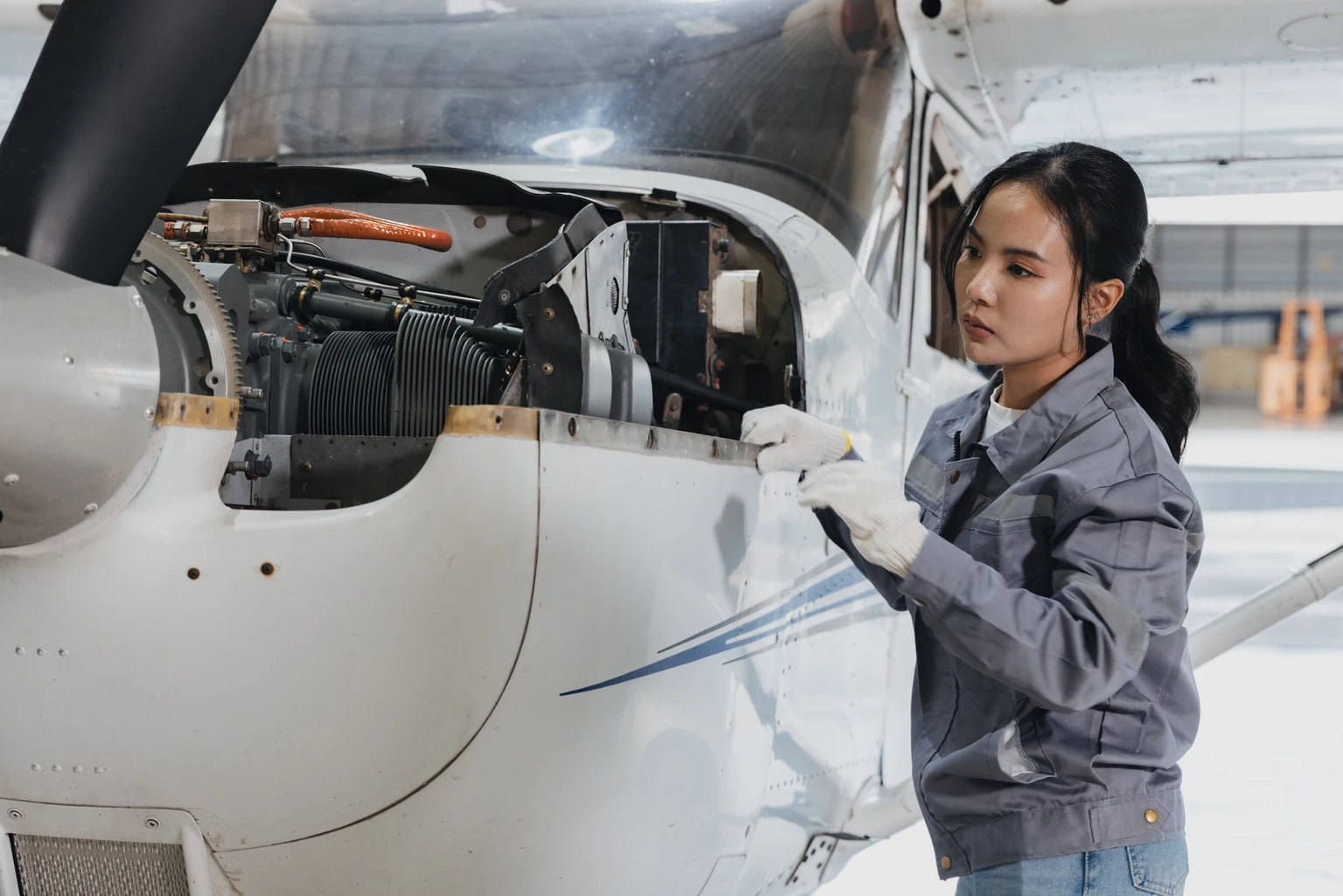 Young female mechanic works on aircraft engine inside spacious hangar during daylight hours