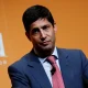 A man in a suit speaking at an event with an orange background.