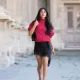 PARIS, FRANCE - APRIL 24: Angela Gonzalez wears long wavy black hair, a red windbreaker jacket by Zara, a black lace-trim mini dress by Zara, a black leather bag by Chanel, black ankle-strap pumps crystal embellished shoes by Jimmy Choo, during a street style fashion photo session, on April 24, 2026 in Paris, France. (Photo by Edward Berthelot/Getty Images)
