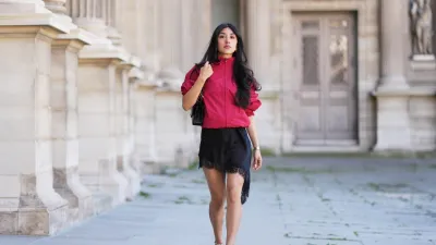PARIS, FRANCE - APRIL 24: Angela Gonzalez wears long wavy black hair, a red windbreaker jacket by Zara, a black lace-trim mini dress by Zara, a black leather bag by Chanel, black ankle-strap pumps crystal embellished shoes by Jimmy Choo, during a street style fashion photo session, on April 24, 2026 in Paris, France. (Photo by Edward Berthelot/Getty Images)