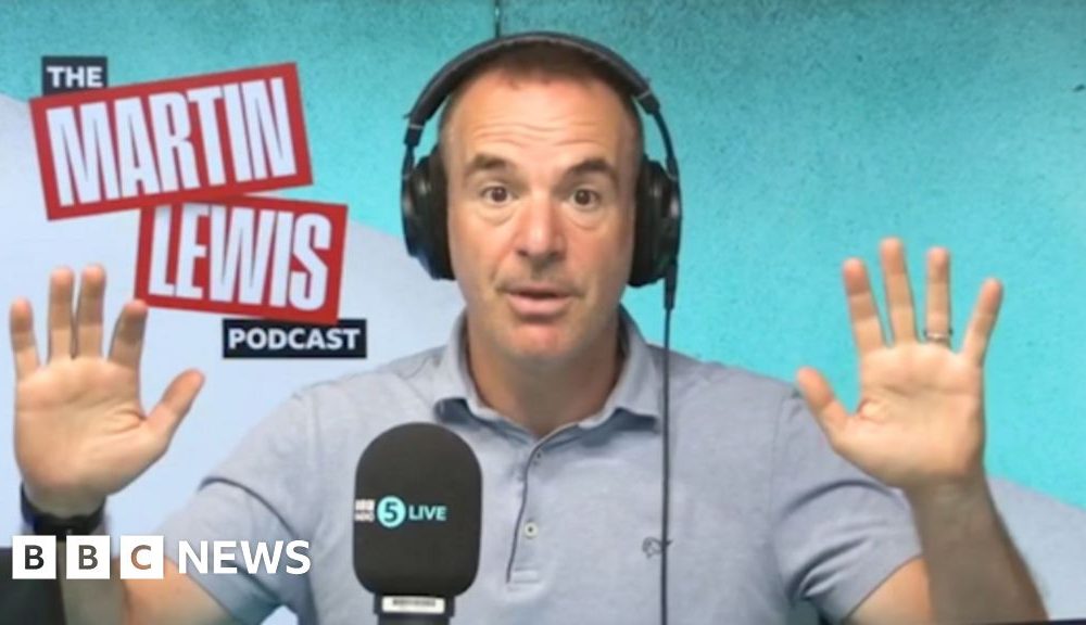 Martin lewis has short day hair, is wearing headphones and a blue polo-shirt and had his hands up to the side of him.