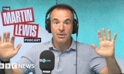 Martin lewis has short day hair, is wearing headphones and a blue polo-shirt and had his hands up to the side of him.
