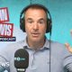 Martin lewis has short day hair, is wearing headphones and a blue polo-shirt and had his hands up to the side of him.