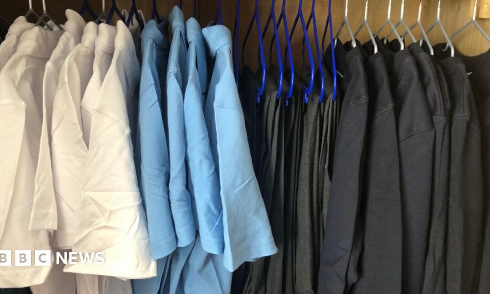 White and light blue polo shirts are hung up on hangers on a rail to the left. On the right are trousers and black jumpers hung up on the same rail.