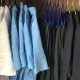 White and light blue polo shirts are hung up on hangers on a rail to the left. On the right are trousers and black jumpers hung up on the same rail.