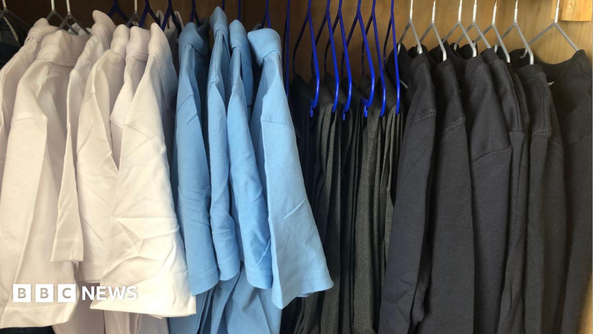 White and light blue polo shirts are hung up on hangers on a rail to the left. On the right are trousers and black jumpers hung up on the same rail.