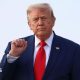 Donald Trump holds up his right fist while wearing a white shirt and red tie.