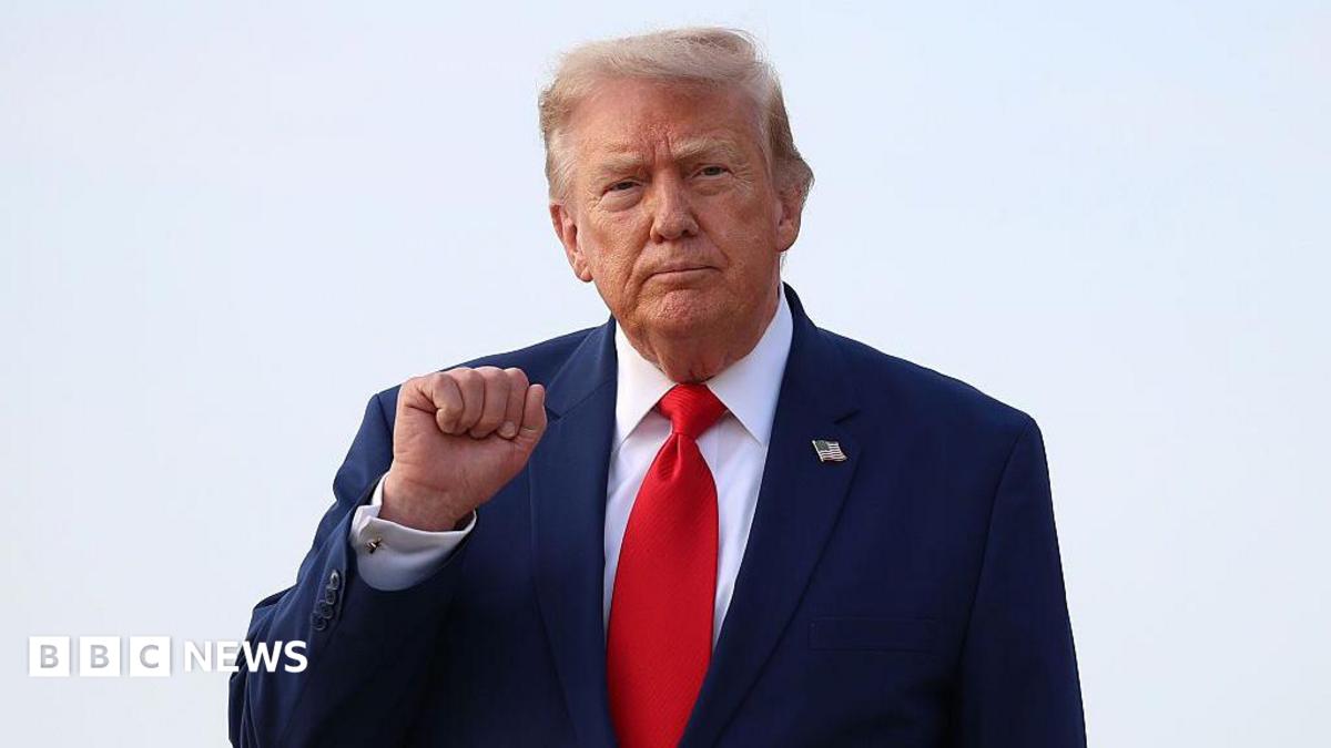 Donald Trump holds up his right fist while wearing a white shirt and red tie.
