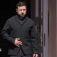 Zelensky, wearing a dark suit, walking through a doorway