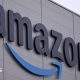 The Amazon logo, which is the world 'Amazon' with its signature stylised arrow underneath, on the side of a grey building with a light overcast sky in the background