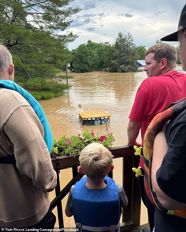 Residents watch the swollen river from higher ground as floodwaters continue to inundate the campground below