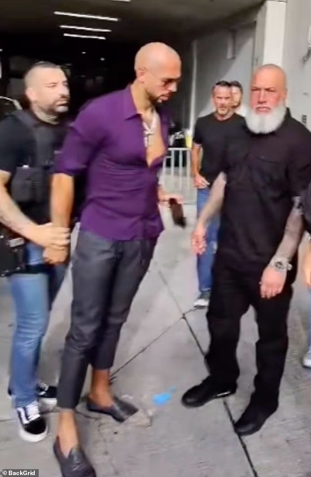 A newly surfaced clip shows Andrew Tate appearing to discreetly pass his phone toward a bodyguard while being placed in handcuff