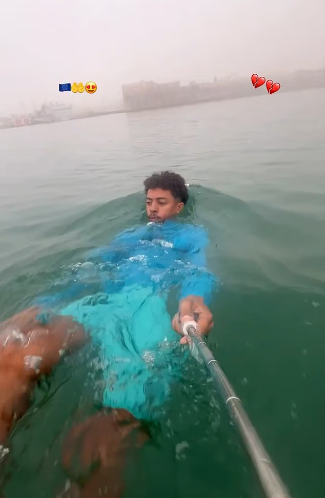 A migrant films himself swimming with a selfie stick as music plays in the background