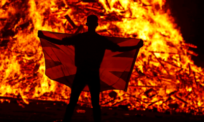 A male holds a flag in front of the Loyalist Corcrain Redmanville bonfire, which was lit to mark the start of the unionist 12 July celebrations, in Portadown, Northern Ireland, on 11 July 2021.