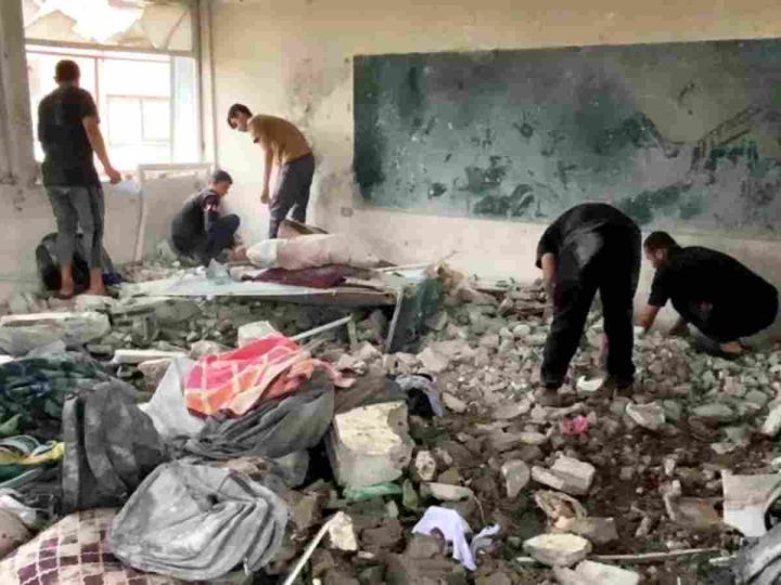 A destroyed classroom in Gaza with men tending to the concrete rubble on the floor