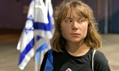 Greta Thunberg looking away, looking displeased, and behind her is an Israel flag crumpled in on itself
