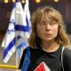 Greta Thunberg looking away, looking displeased, and behind her is an Israel flag crumpled in on itself