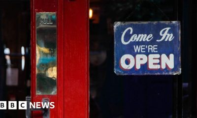 A red pub door with a 'Come in we're open' sign