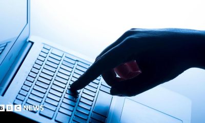 A hand with index finger outstretched pressing a key in the middle of a laptop keyboard.