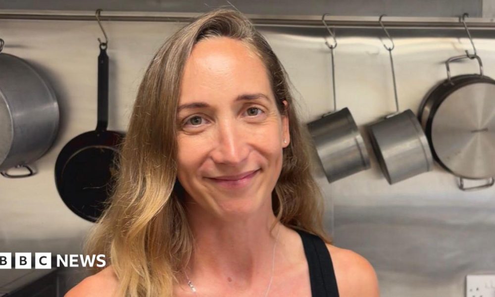 Lady stood in a kitchen in front of pots and pans.