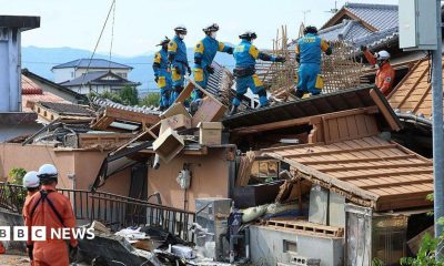 Rescue workers in overalls stand on top of a collapsed house