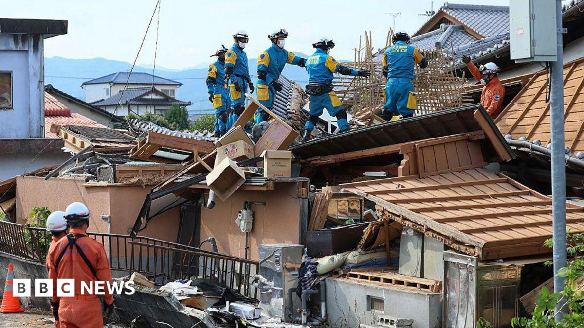 Rescue workers in overalls stand on top of a collapsed house