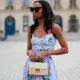 PARIS, FRANCE - APRIL 29: Emilie Joseph wears black large sunglasses, crystal earrings, a pale blue with red / green / navy blue / beige flower print pattern heart neck / tank-top / belted / midi dress, a beige wickers and white shiny leather bi-material handbag, during a street style fashion photo session, on April 29, 2023 in Paris, France. (Photo by Edward Berthelot/Getty Images)