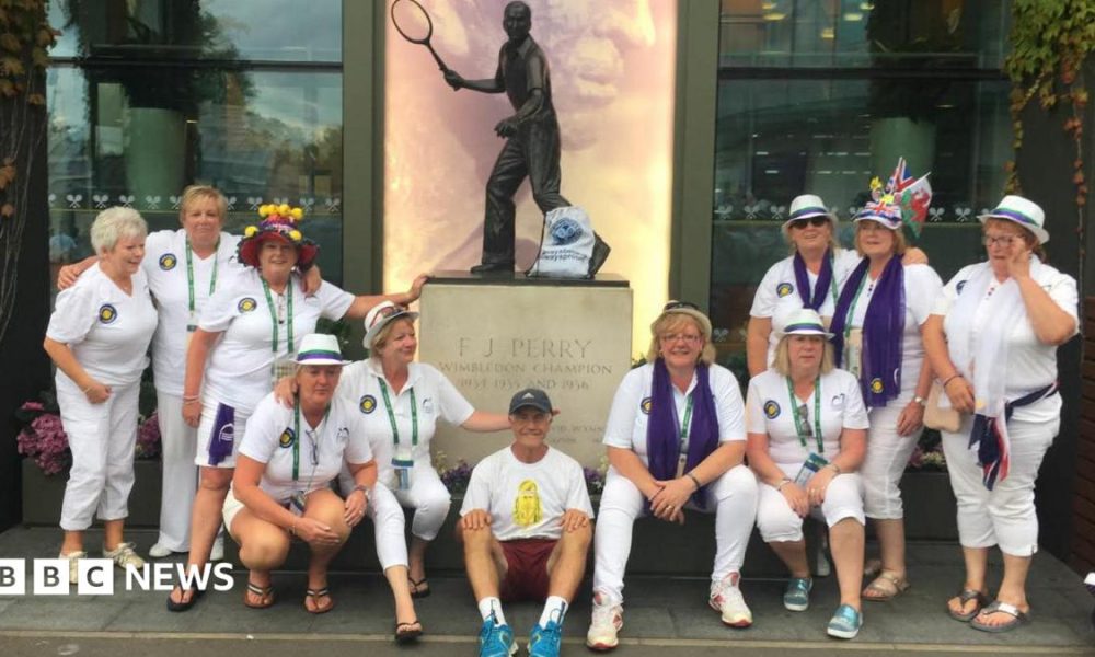 Geoff Hughes is sitting in the middle of a photo in front of a Fred Perry statue surrounded by members of the Andy Murray fan group The Murraynators