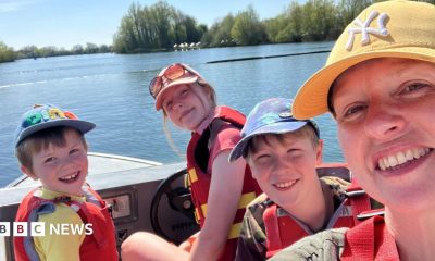 A woman wearing a yellow cap and three children, on a boat. All are wearing life jackets, and the photo is taken as a selfie-style with everyone looking at the camera