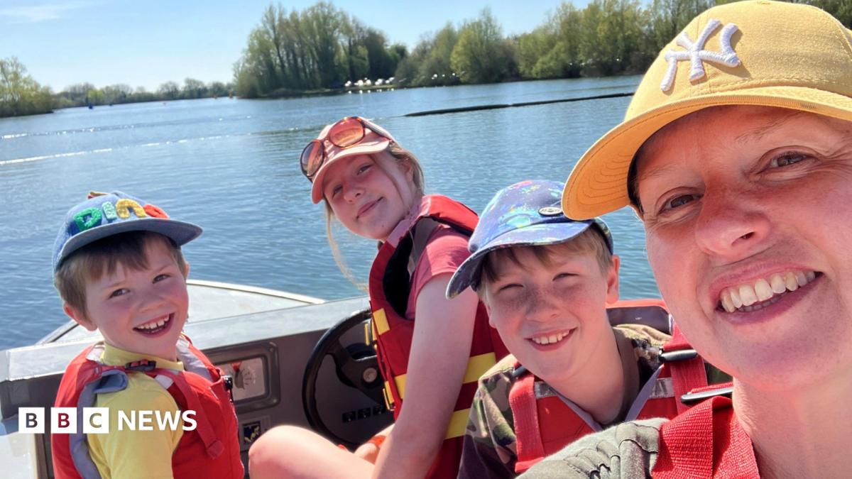 A woman wearing a yellow cap and three children, on a boat. All are wearing life jackets, and the photo is taken as a selfie-style with everyone looking at the camera