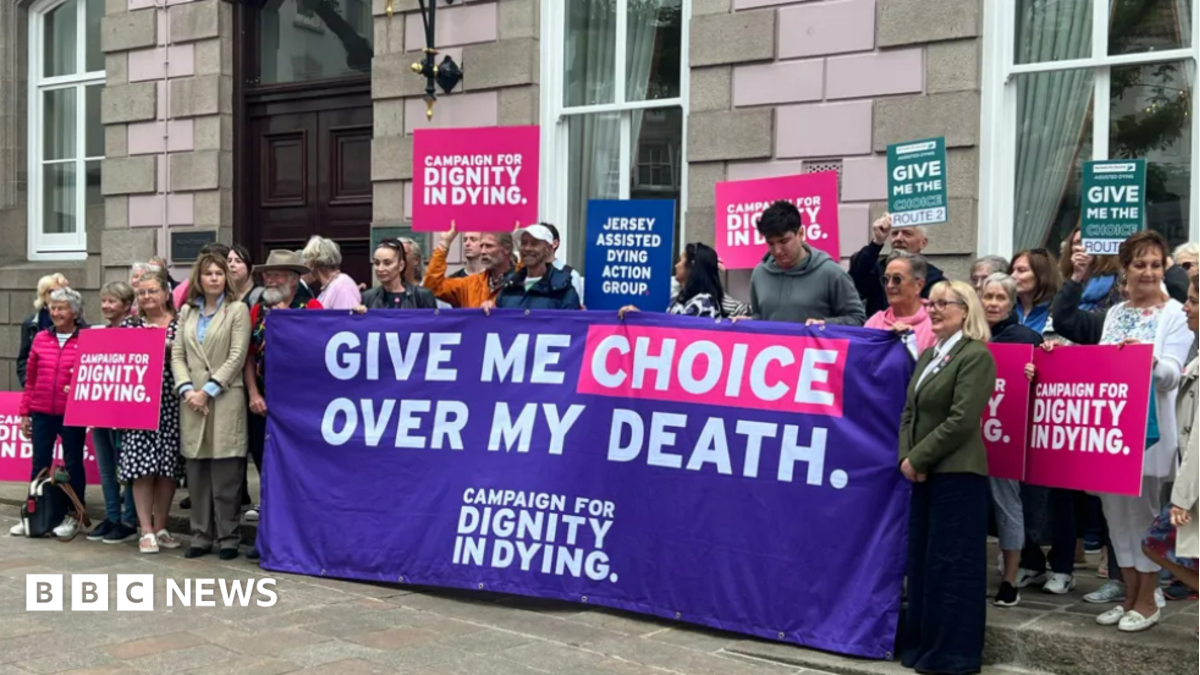 Campaigners for assisted dying holding a large purple "Give me choice over my death" and placards outside a grey building, the States Chamber.