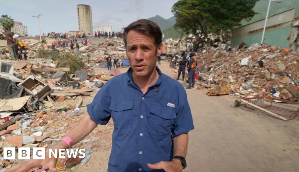 Man in blue shirt walking among rubble after earthquake