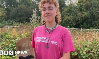 Alex Vardill wearing a pink T-shirt, smiling straight at the camera and holding a box of blackberries.