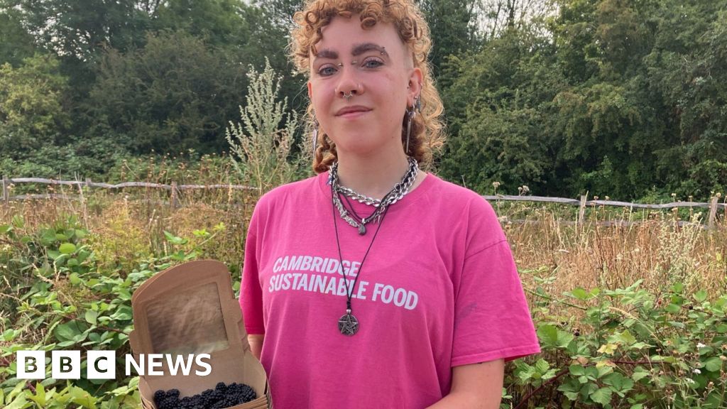 Alex Vardill wearing a pink T-shirt, smiling straight at the camera and holding a box of blackberries.