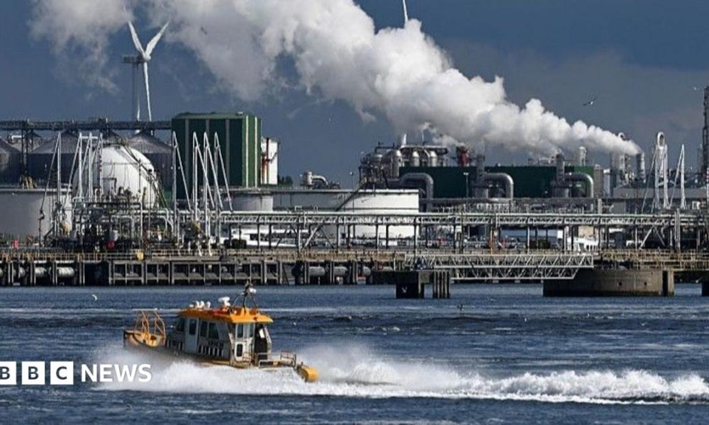 An oil refinery at the Port of Rotterdam. In the foreground a small boat leaves a wake in the water.