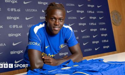 Quenda resting his arms on a table with a Chelsea shirt on and in front of him after signing for the club